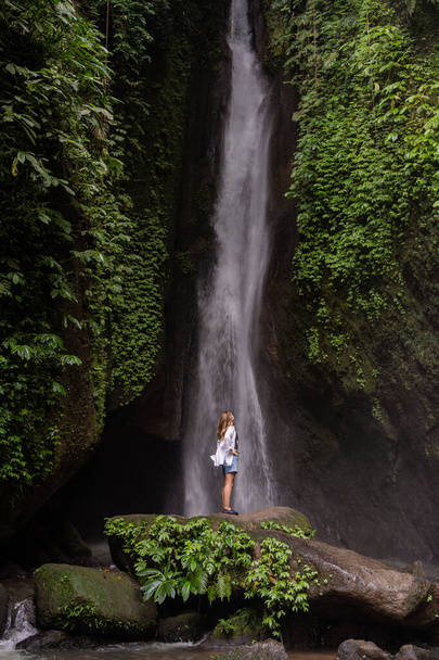 A woman standing in front of waterfall in the jungle. Travel Indonesia. Hidden beauty of the island - Фото, зображення