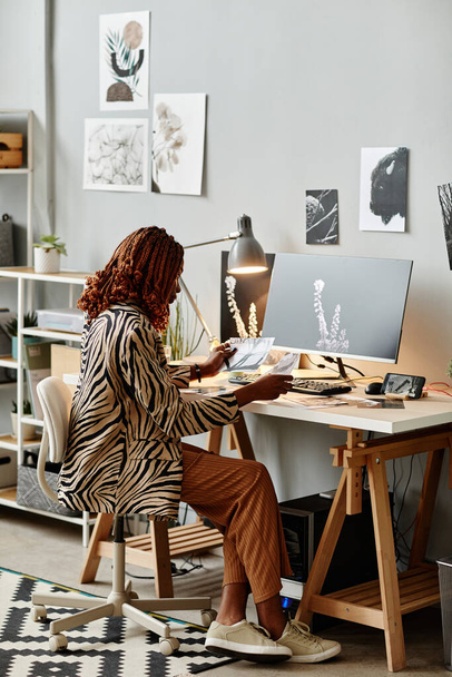 Вертикальний повнометражний знімок молодої жінки-творця на робочому місці домашнього офісу з графічними принтами - Фото, зображення
