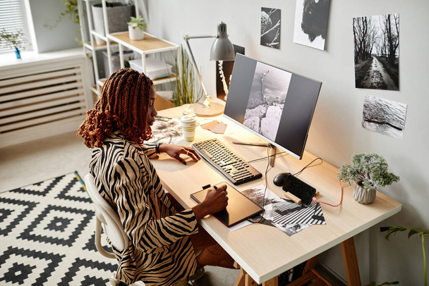 Portrait grand angle de créatrice noire éditant des photographies au bureau à domicile avec des impressions graphiques, espace de copie - Photo, image