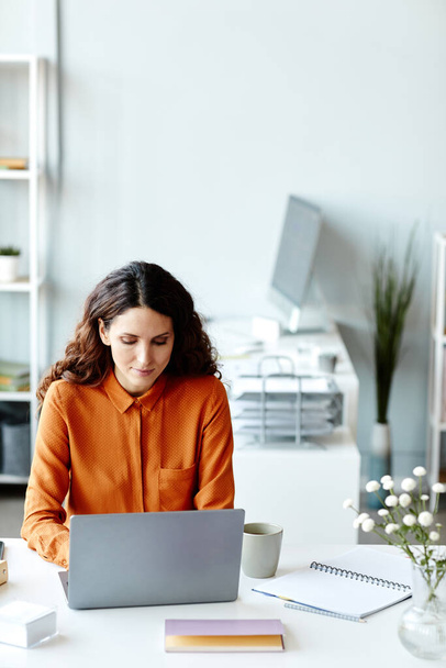 Вертикальный снимок современной молодой взрослой женщины-менеджера, работающей над бизнес-проектом на ноутбуке в офисе - Фото, изображение