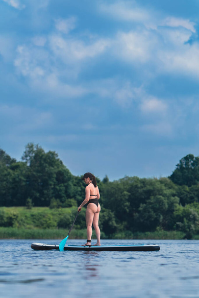 aantrekkelijke vrouw in badmode op supboard in het midden van het meer - Foto, afbeelding