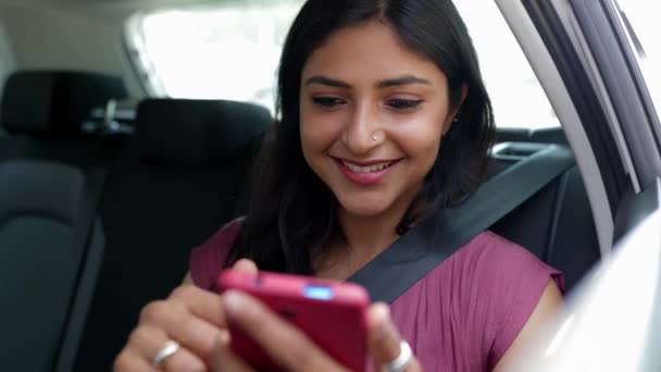 Joyeux jeune Indienne utilisant un téléphone portable assis sur le siège arrière d'une voiture. Concept de technologie et de transport. - Séquence, vidéo