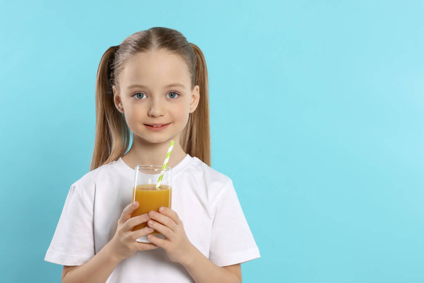 Cute little girl holding glass of fresh juice with straw on light blue background, space for text - Photo, image