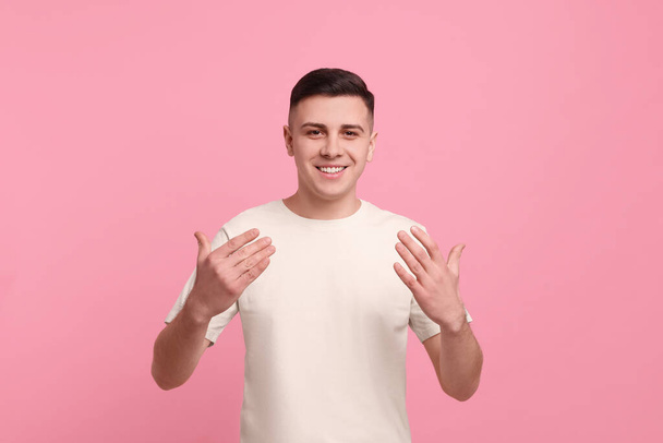 Handsome man inviting to come in against pink background - Foto, imagen