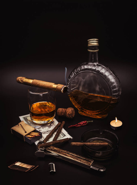 Quality cigars with cognac, cutter, 100 dollar paper, ashtray, light candle, photo film and red hot pepper on black background - Φωτογραφία, εικόνα
