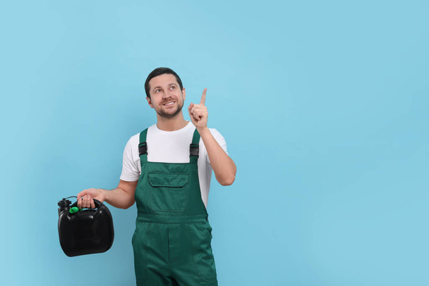 Man holding black canister and pointing at something on light blue background. Space for text - Foto, imagen