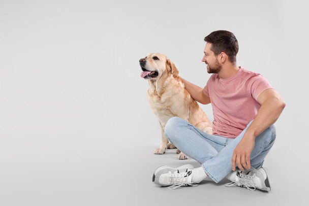 Man with adorable Labrador Retriever dog on light gray background, space for text. Lovely pet - Photo, Image