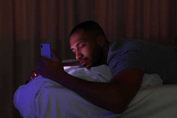 Young man sleeping while holding smartphone in bed at night. Internet addiction - Foto, Imagen