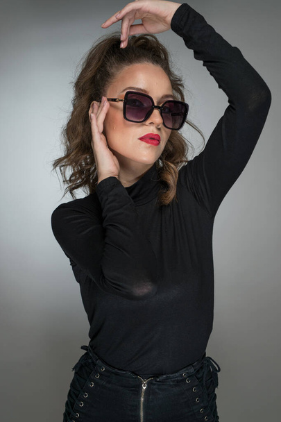 Woman with sunglasses  and black blouse against a grey background. Style beauty girl with red lips.Portrait of stunning young woman in sunglasses look into the camera - Fotografie, Obrázek