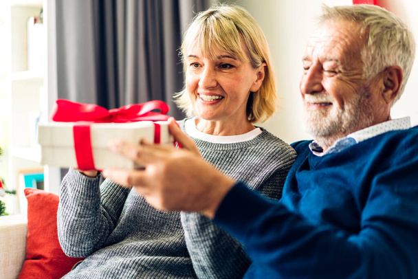 Romantic sweet senior couple having fun and smiling while celebrating enjoying valentines day time together.Senior man giving gift box surprise to wife in valentines day at home - Photo, Image