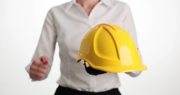 Female person knocking on helmet stands on light background. Woman in white shirt demonstrates durability of protection. Safety equipment - Footage, Video