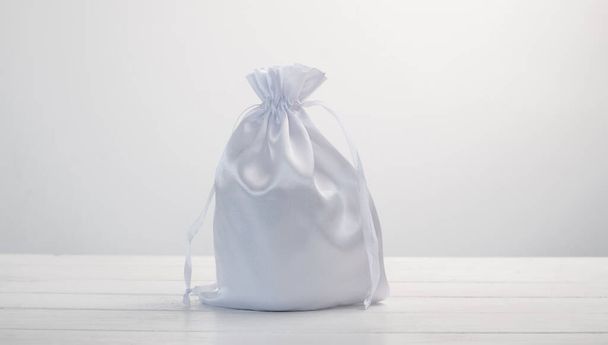 White gift bag made with silk material on white background. Stylish soft pouch with present inside - Foto, Imagem