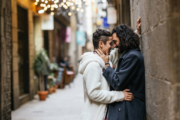 Un par de hombres apasionados besándose en la calle, callejón con restaurantes al fondo. - Foto, Imagen