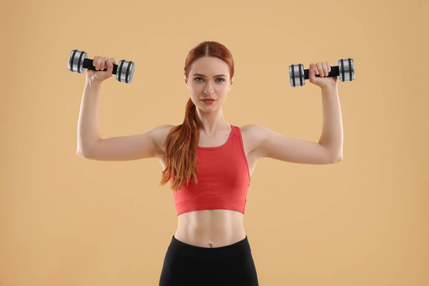 Young woman in sportswear doing exercises with dumbbells on beige background - Foto, immagini