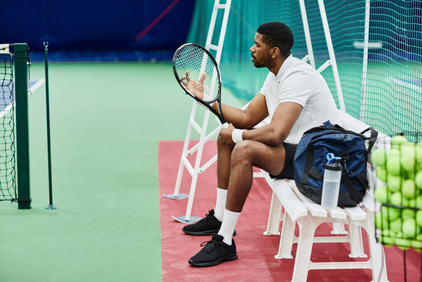 Retrato de vista lateral del jugador de tenis profesional que sostiene la raqueta mientras toma un descanso en el banco en la corte, espacio para copiar - Foto, Imagen