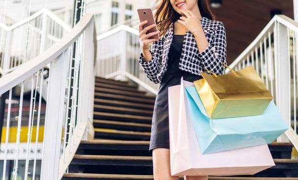Portré mosolygós szépség ázsiai divat boldog nő pihenjen, és élvezze a vásárlás ideje nyári eladás séta és gazdaság színes táska vásárolni valamit vásárol használja okostelefon a boltban - Fotó, kép