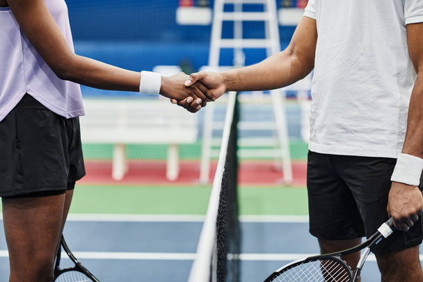 屋内コートで試合中にネット上で握手をする2人のテニス選手のサイドビュー - 写真・画像
