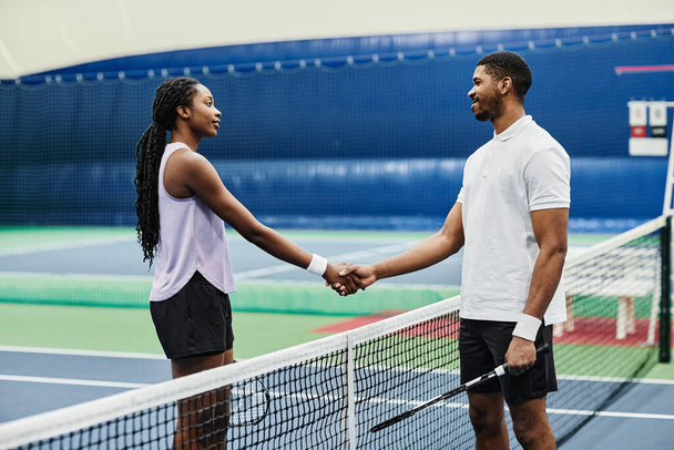 Portrait latéral de deux joueurs de tennis serrant la main sur le filet pendant le match à l'intérieur du terrain, espace de copie - Photo, image