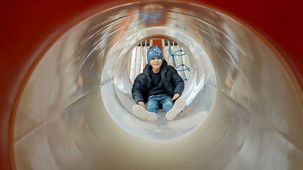 公共の遊び場でチューブスライドを滑る小さな少年. 幸せな子供たち,楽しいアウトドア,公園でのレジャー - 写真・画像