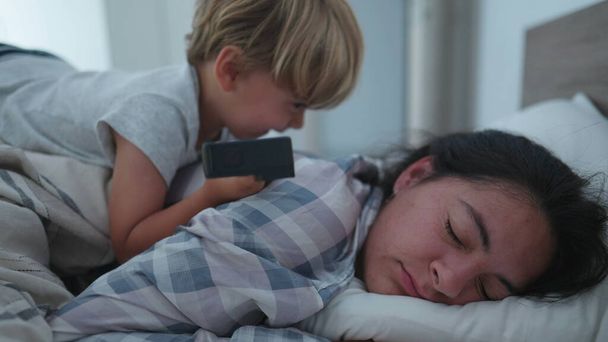 child waking up mother in morning bed jumping on top mom - 写真・画像