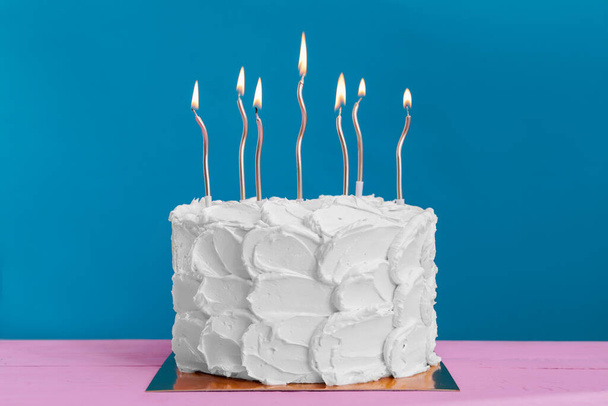 Delicious cake with cream and burning candles on pink wooden table - 写真・画像