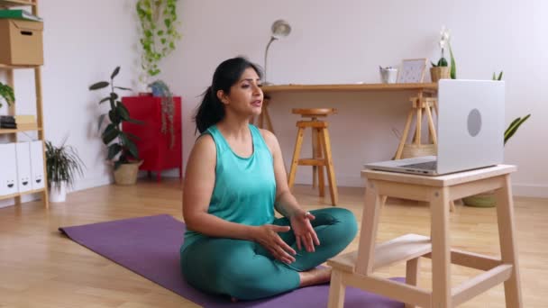 若い先住民のインド人女性ヨガインストラクターは、自宅のスタジオからノートパソコンを使用してビデオ通話を介して呼吸や瞑想をオンライン演習を教えています。健康的なライフスタイルのコンセプト. - 映像、動画