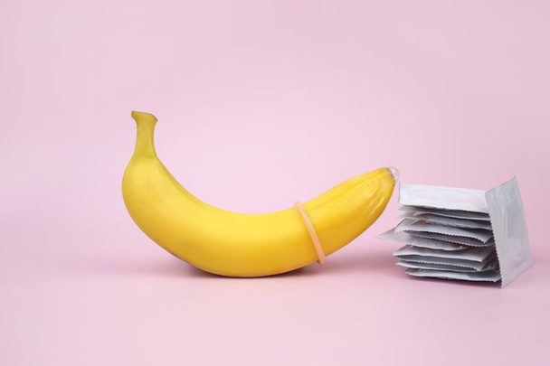 Condón y plátano sobre un fondo rosa de cerca. El concepto de salud sexual. - Foto, imagen