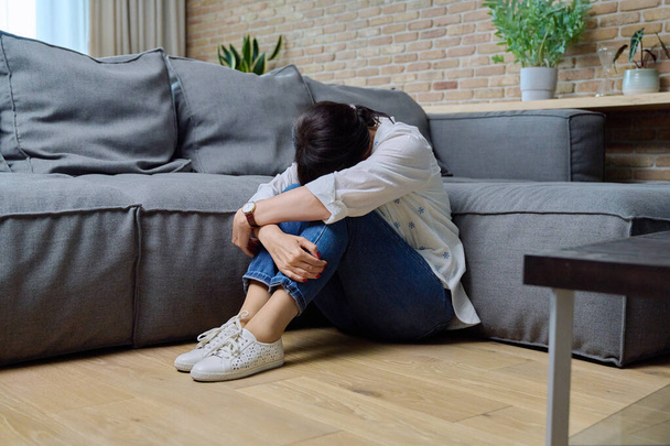 Mature woman suffering from physical pain, mental problems. 50s female sitting at home on floor in living room near sofa. Problems difficulties stress loneliness, age-related changes, health concept - Foto, Bild