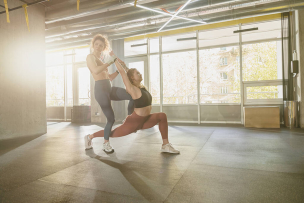 Fit woman doing stretching exercises with the help of personal trainer at gym. High quality photo - Fotografie, Obrázek