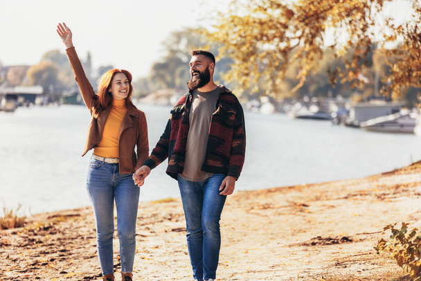 Szczęśliwa młoda para w miłości trzymając się za ręce i spacerując po wybrzeżu w pobliżu rzeki.  - Zdjęcie, obraz