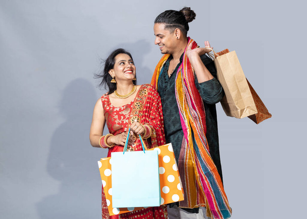 Ευτυχισμένο ζευγάρι Ινδιάνων που φοράνε παραδοσιακά ρούχα κρατώντας τσάντες για ψώνια και γιορτάζοντας το φεστιβάλ Ντιβάλι μαζί. - Φωτογραφία, εικόνα