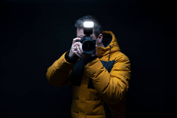 Portré egy fotós sárga télikabátban fotózás vaku egy fekete háttér stúdió - Fotó, kép