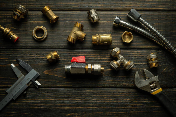 Ersatzteile und Beschläge mit Werkzeug auf einem schwarzen Vintage-Tisch. Vorbereitung auf die Reparatur von Sanitär-Armaturen oder Sanitär. - Foto, Bild