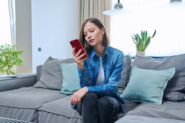 Young fashionable beautiful woman at home on couch in living room using smartphone. Internet online service, technology, mobile applications for study leisure life work shopping - Fotó, kép