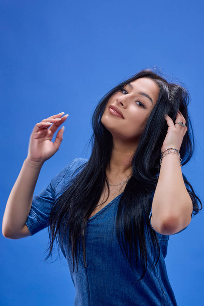 a young brunette with long hair posing in the studio isolated on a blue background - Zdjęcie, obraz