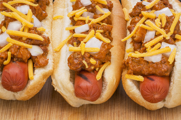 Tre deliziosi hot dog chili su un tagliere di legno
 - Foto, immagini