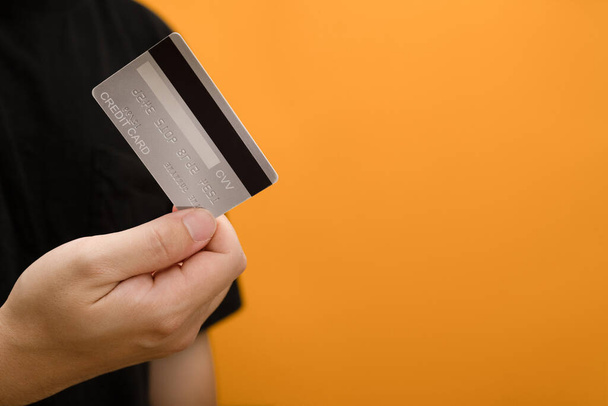 Hombre sosteniendo tarjeta de crédito sobre fondo amarillo con espacio vacío. Personas, transacciones sin efectivo, compras y finanzas. - Foto, Imagen