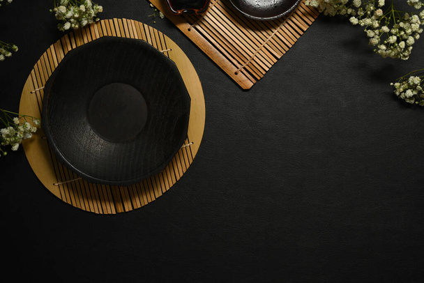 Leerer schwarzer Schieferteller und getrocknete Blumen auf schwarzem Steintisch für Menü, Rezept und Restaurantgericht. - Foto, Bild