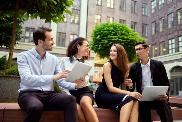 Group of employees, colleagues sitting on bench outside office, working, talking, discussing projects. Teamwork. Concept of business, career development, ambitions, success, office lifestyle - 写真・画像
