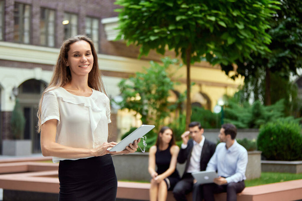 Focus on smiling businessman, employee standing outside office with tablet. Blurred people on background. Concept of business, career development, ambitions, success, office lifestyle - Fotografie, Obrázek