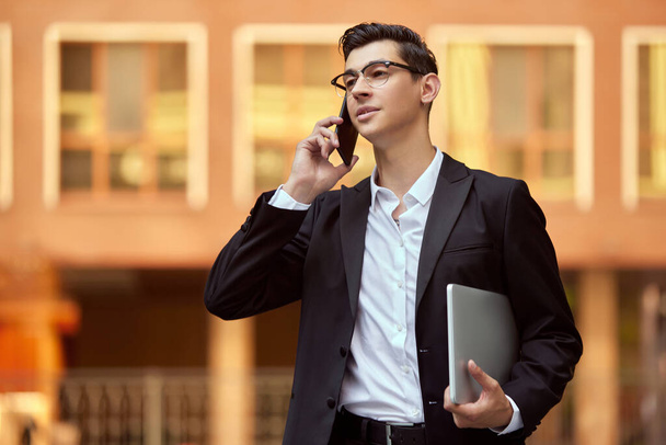 Confident, concentrated businessman in formal wear walking along street outside office and talking on mobile phone. Concept of business, career development, ambitions, success, office lifestyle - Φωτογραφία, εικόνα