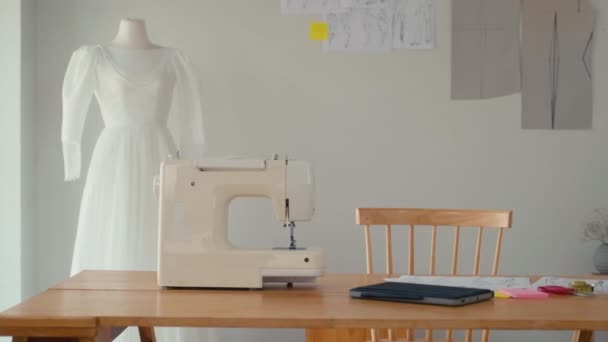 Medium shot van riool bureau met naaimachine en digitale tablet, witte jurk en schetsen op de achtergrond - Video
