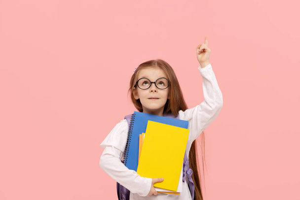 Portrait of a schoolgirl with textbooks and a backpack on a pink background points up. Back to school - Foto, imagen