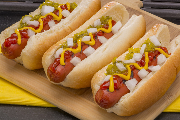 Tres deliciosos hot dogs con mostaza, ketchup, cebolla y encurtidos
 - Foto, imagen