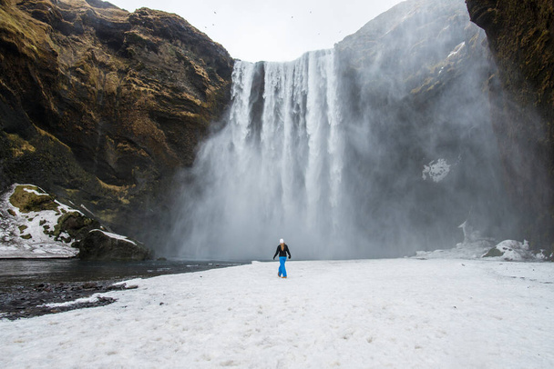Турист стоїть перед Скогафосом один з найвідоміших водоспадів на півдні Ісландії протягом зимового сезону. - Фото, зображення