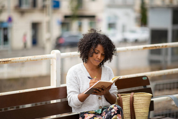 Portrait young woman sitting with book outdoor - Photo, image