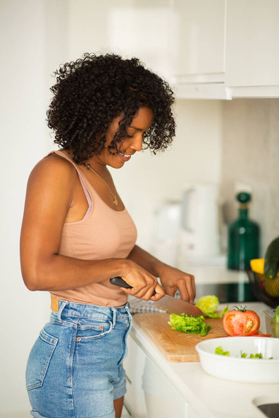 Portrait jeune femme afro-américaine coupant la nourriture dans la cuisine - Photo, image