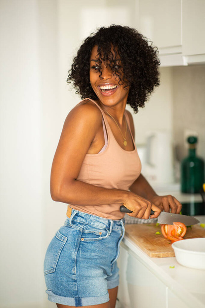 Portrait heureuse jeune femme afro-américaine coupant des légumes dans la cuisine - Photo, image