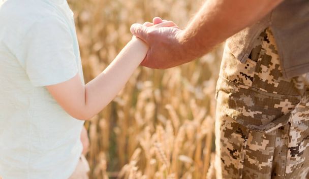 Military man and child holding hands in wheat field at sunset. Ukraine independence day concept. Stop war in Ukraine. Save Ukraine - Photo, image