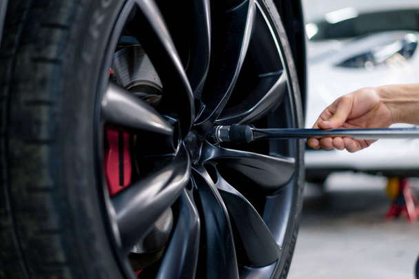 Auto mechanic man changing a wheel on a luxury white car using balloon wrench at a car service station close-up - Photo, Image
